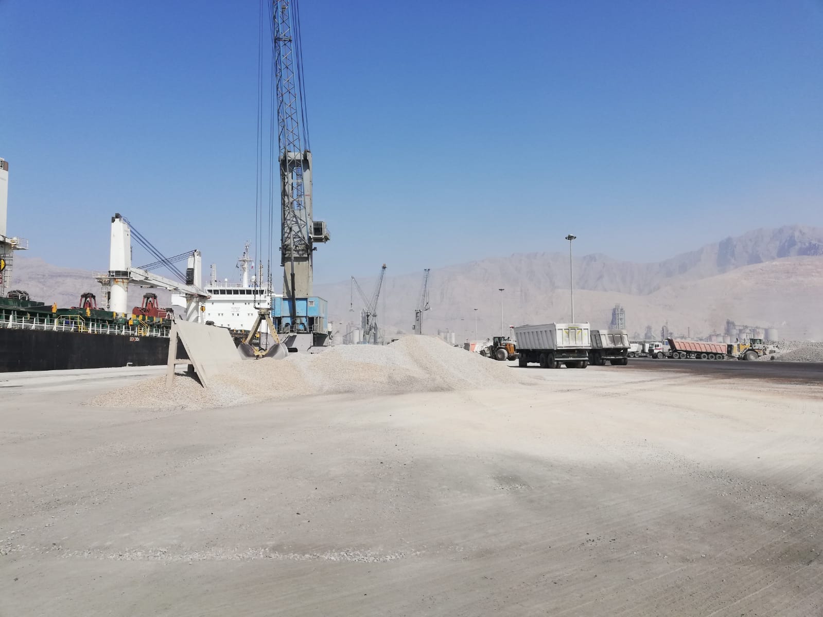 Stockpiled bulk cargo beside a vessel and shore crane