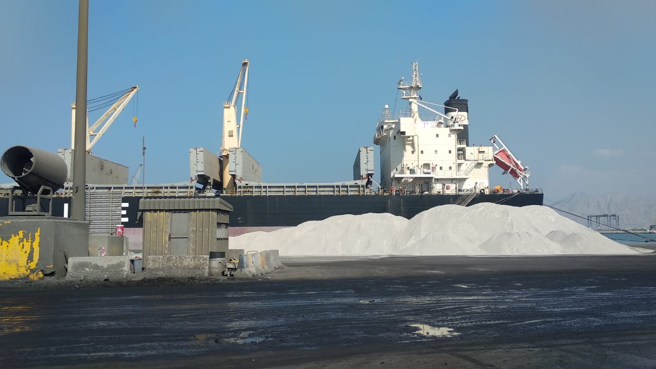 Bulk vessel alongside a white cargo stockpile