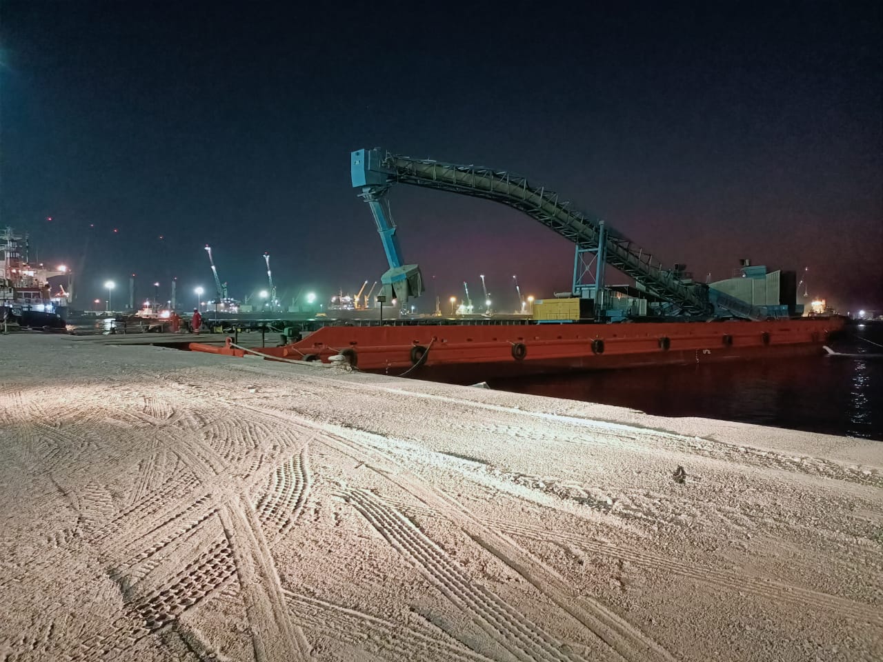 Cargo conveyor and vessel viewed across a stockpile at night