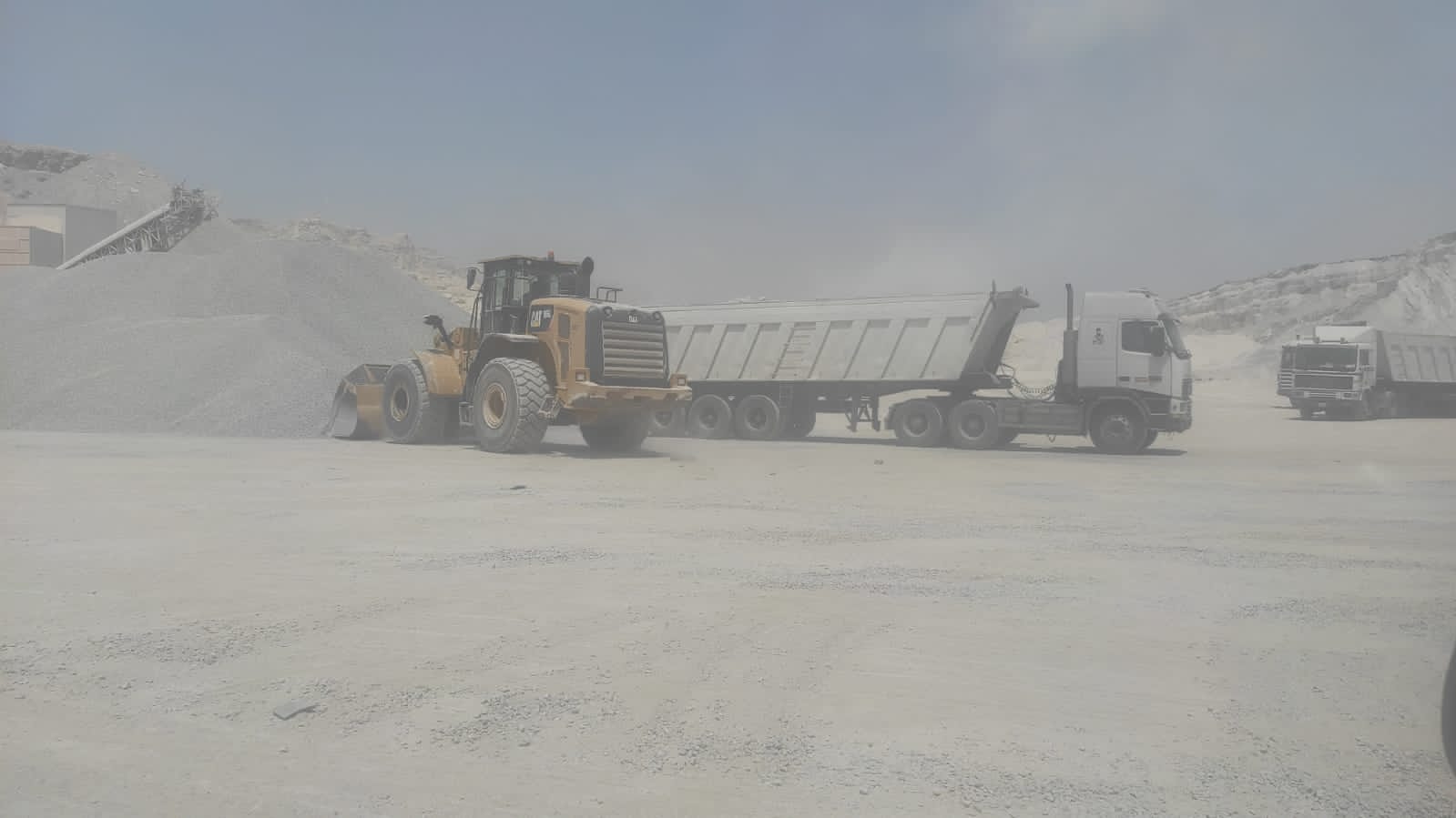 Wheel loader and trucks working among bulk cargo stockpiles